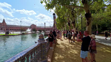 Tourists-walk-around-Plaza-de-España-Sevilla-Spain-landmark-Andalucia-travel-destination,-taking-pictures-of-colonial-architecture-next-to-clean-river