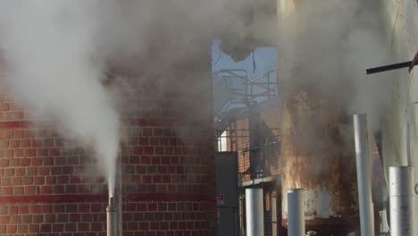 Aufsteigender-Rauch-Aus-Industrierohren-Vor-Einem-Gebäude-Mit-Klarem-Himmel,-Städtische-Umgebung