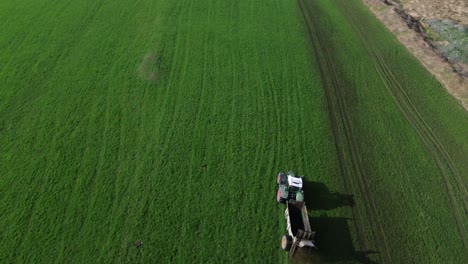 Toma-Aérea-De-Un-Tractor-Rociando-Estiércol-En-Un-Campo-De-Hierba-Verde-Con-Montañas-Nevadas-En-El-Fondo