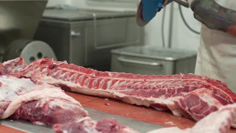 Butcher-cutting-through-pig-ribs-with-automated-saw-for-ribeye-steak