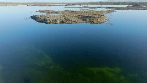Sharp-jagged-limestone-rocks-protrude-from-flooded-mossy-waters-in-the-Burren-Ireland,-aerial-dolly-on-sunny-day
