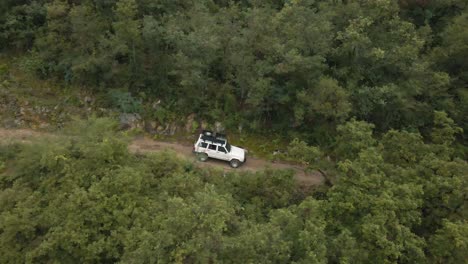 White-Cherokee-truck-on-an-adventure-driving-trough-the-woods-in-the-mountains,-aerial-drone-shot