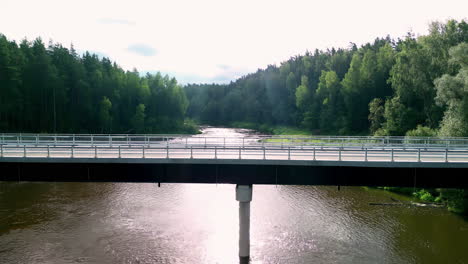 Luftbild-Panoramadrohne,-Herauszoomen,-Asphaltierte-Brückenstraße-über-Dem-Flusskanal,-Wald-Aus-Grünen-Kiefern-Und-Blauer-Skyline-Rund-Um-Den-Landtransport,-Der-Den-Wasserkanal-überquert