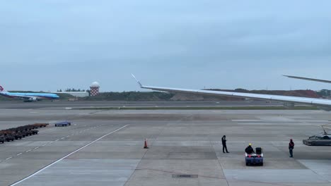 Bodenpersonal-Signalisiert-Einem-Großen-Flugzeug-Auf-Dem-Rollfeld-Eines-Flughafens,-Bedeckter-Himmel,-Regen-Möglich