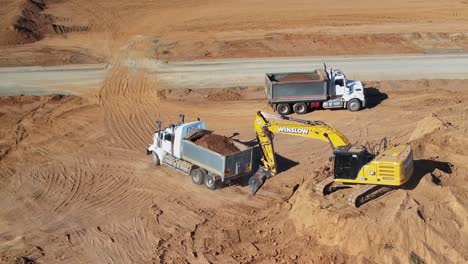 Yarrawonga,-Victoria,-Australia---8-March-2024:-Tip-truck-driving-away-from-dirt-stockpile-after-excavator-has-loaded-dirt-at-Silverwoods-Estate-in-Yarrawonga