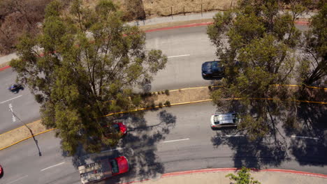 Eine-Kurvige-Straße-Mit-Autos-Und-Umliegenden-Bäumen,-Die-Schatten-Werfen,-Luftaufnahme