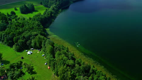 Beautiful-lake-in-green-forest,-people-camping-and-boats-on-lake-shore