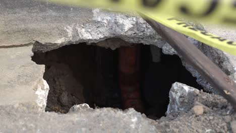 Exposed-Sewage-Pipe-from-Sink-Hole-with-Yellow-Precaution-Tape-in-Foreground