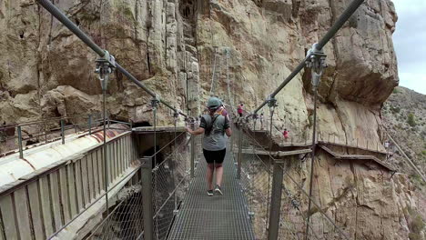 Woman-walking-across-hanging-bridge-of-Gaitanes-Gorge-on-the-Caminito-del-Rey-in-Ardales,-Malaga