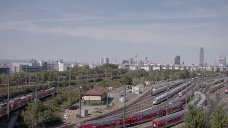 Panoramic-view-of-Frankfurt's-railway-station-with-multiple-trains-and-urban-skyline-in-the-background,-daytime