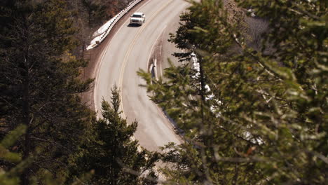 A-truck-drives-along-a-winding-mountain-road-in-the-forest,-long-lens
