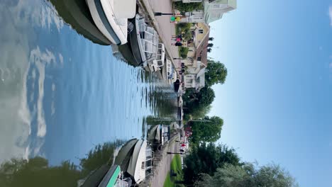 Vertical-shot-of-boats,-people-and-houses-by-river-in-Trosa,-Sweden