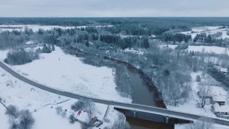Abava-river-winding-through-a-snowy-landscape-near-Renda-village-,-winter-setting,-aerial-view,-moving-backward,-tilt-down