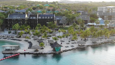 Sunbeds-on-beach-at-seaside-resort-on-Curaçao-island,-aerial-pull-out