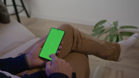 Man-Sitting-on-his-Sofa-in-conversation,-receives-notification-on-his-smartphone,-green-screen