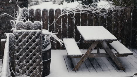 Snow-falling-on-fence,-bench-and-table