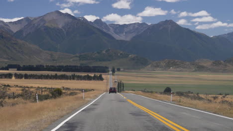 Slow-Motion-shot-of-a-car-driving-down-a-road-towards-mountains---Arthur's-Pass,-New-Zealand