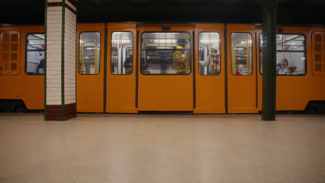 Passengers-getting-on-the-metro,-subway-leaving-the-station,-people-travelling-on-the-M1-underground-in-Budapest,-Hungary,-tube,-the-oldest-metro-line-in-Europe,-old-Hungarian-public-transportation