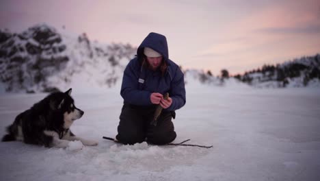 Ein-Mann-Hat-Beim-Eisfischen-Mit-Seinem-Hund-In-Bessaker,-Provinz-Trondelag,-Norwegen,-Erfolgreich-Einen-Fisch-Gefangen-–-Statische-Aufnahme