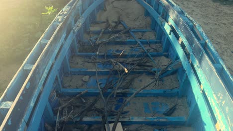 An-aged-fishing-boat-resting-in-a-coastal-locale,-partly-buried-in-the-sand-with-remnants-of-wooden-branches,-evoking-the-quaint-aesthetics-of-a-fishing-village-scene