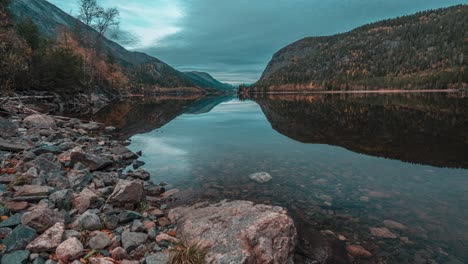 Dunkle-Herbstwolken-Und-Bewaldete-Hügel-Spiegeln-Sich-In-Der-Noch-Spiegelglatten-Oberfläche-Des-Bergsees