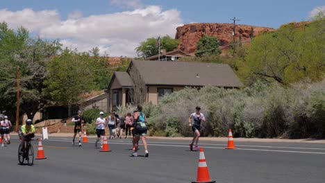 Slow-motion-shot-of-people-running-and-racer-biking-in-front-of-house-and-red-landscape-at-the-Intermountain-Health-IRONMAN-70