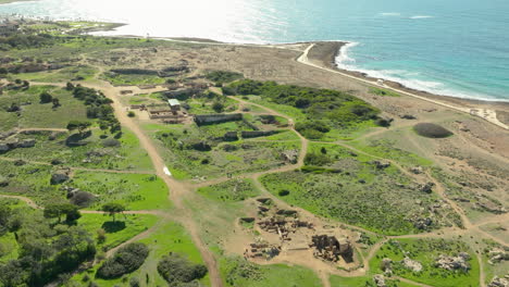 An-overhead-shot-of-the-Tombs-of-the-Kings,-displaying-the-sprawling-archaeological-site-with-well-preserved-ruins,-greenery,-and-walking-paths-near-the-coastline