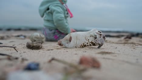 Closeup-of-a-plastic-bottle-on-a-beach-with-a-baby-sitting-in-the-background