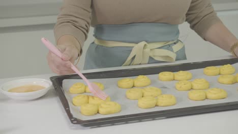 Cerca-De-La-Mano-De-Un-Chef-Aplicando-Yema-De-Huevo-Con-Un-Cepillo-Sobre-Masa-De-Pan-Moldeada-En-La-Mesa-De-La-Cocina.