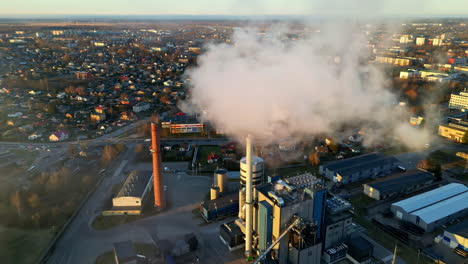 Smoking-factory-chimneys,-polluting-in-a-sunlit-urban-community---Aerial-view