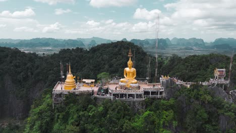 Drone-shot-of-Wat-Tham-Suea-in-Krabi,-a-Buddhist-temple-nestled-in-a-cave-complex-with-stunning-views-and-a-giant-golden-Buddha-statue