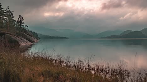 Rays-of-the-setting-sun-shine-through-the-stormy-clouds-whirling-over-the-lake-and-a-forest-in-a-timelapse-video