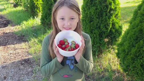 Cute-young-girl-holding-bowl-of-strawberry-outdoors,-sunny-warm-day