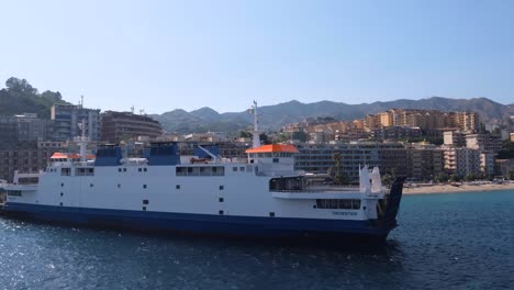 Tracking-Wide-Shot-of-Italian-Ship-Surrounded-by-Bright-Blue-Water---Colorful-Beach-Hotels-on-Sunny-Day