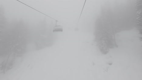 Riding-a-chairlift-in-heavy-fog-in-a-snowy-forest-in-the-Alps,-Europe