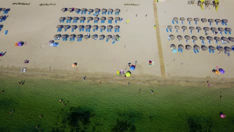 Kipp-Drohnenaufnahme-Des-Strandes-Playa-Del-Port-De-Pollenca,-Zeigt-In-Reihen-Aufgereihte-Sonnenschirme,-Unter-Denen-Strandbesucher-Auf-Der-Spanischen-Insel-Mallorca-Ein-Sonnenbad-Nehmen