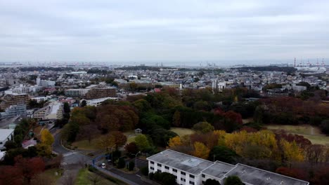 A-sprawling-cityscape-with-patches-of-autumn-trees-and-cloudy-skies,-daytime,-aerial-view