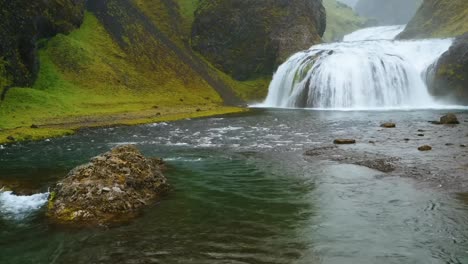 Eine-Weitwinkel-4k-Aufnahme-Eines-Kaskadierenden-Isländischen-Wasserfalls,-Umgeben-Von-Einer-Grünen-Berglandschaft