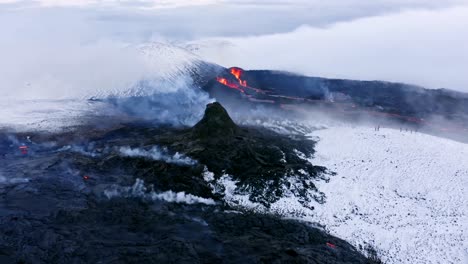 A-4K-drone-captured-a-dramatic-and-unique-aerial-view-of-a-landscape-featuring-white-snow,-black-lava-formations,-fog,-and-glaciers,-with-volcanic-lava-erupting-at-its-center