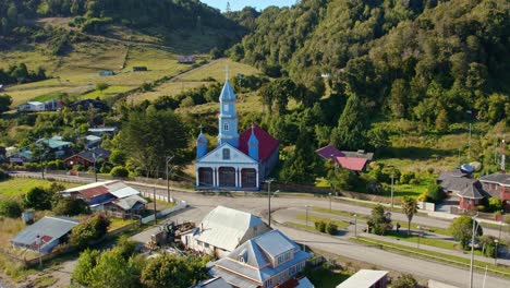 Tenaun-village-with-iconic-blue-unesco-heritage-church-in-chiloe,-sunny-day,-aerial-view