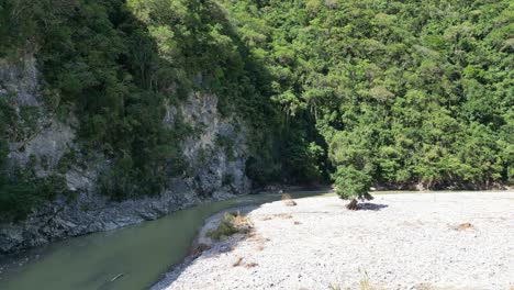 Drone-flying-over-riverbank-at-Muchas-Aguas,-San-Cristobal-in-Dominican-Republic