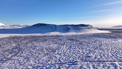 Hverfjall-volcano,-surrounded-in-snow,-on-a-clear-day,-aerial-forward-approach