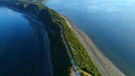 Drone-circling-a-road-in-middle-of-a-steep-culmen-ridge-in-sunny-Chiloe,-Chile