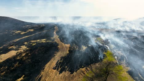 Smoke-billowing-off-freshly-burnt-prairie-after-controlled-burn-in-the-Flint-Hills-of-Kansas,-Drone-Shot