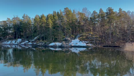 Das-Wasser-Der-Ostsee-Spiegelt-Kiefern,-Einen-Schimmernden-Blauen-Himmel-Und-Schnee-Im-Winter-Oder-In-Der-Nebensaison-Im-Frühjahr-Wider