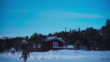 A-Man-Strides-Toward-the-Wooden-Cabin-Nestled-in-the-Snowy-Landscape-in-Bessaker,-Trondelag-County,-Norway---Static-Shot