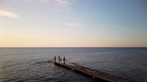 Kinder-Springen-Bei-Sonnenuntergang-In-Schweden-Vom-Steg-Am-Offenen-Meer-Ins-Wasser