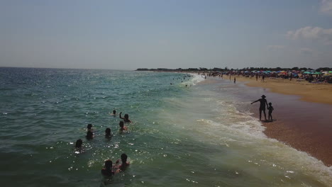 Drone-panning-forward-shot-of-ocean-with-waves-breaking-and-vacationers-at-the-beach