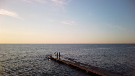 Kinder-Schwimmen-Und-Klettern-Bei-Sonnenuntergang-Auf-Einer-Leiter-Am-Steg-Am-Offenen-Meer-Hinauf