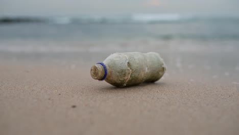 Una-Botella-De-Plástico-Tirada-En-La-Playa-Con-Olas-Rompiendo-En-El-Fondo